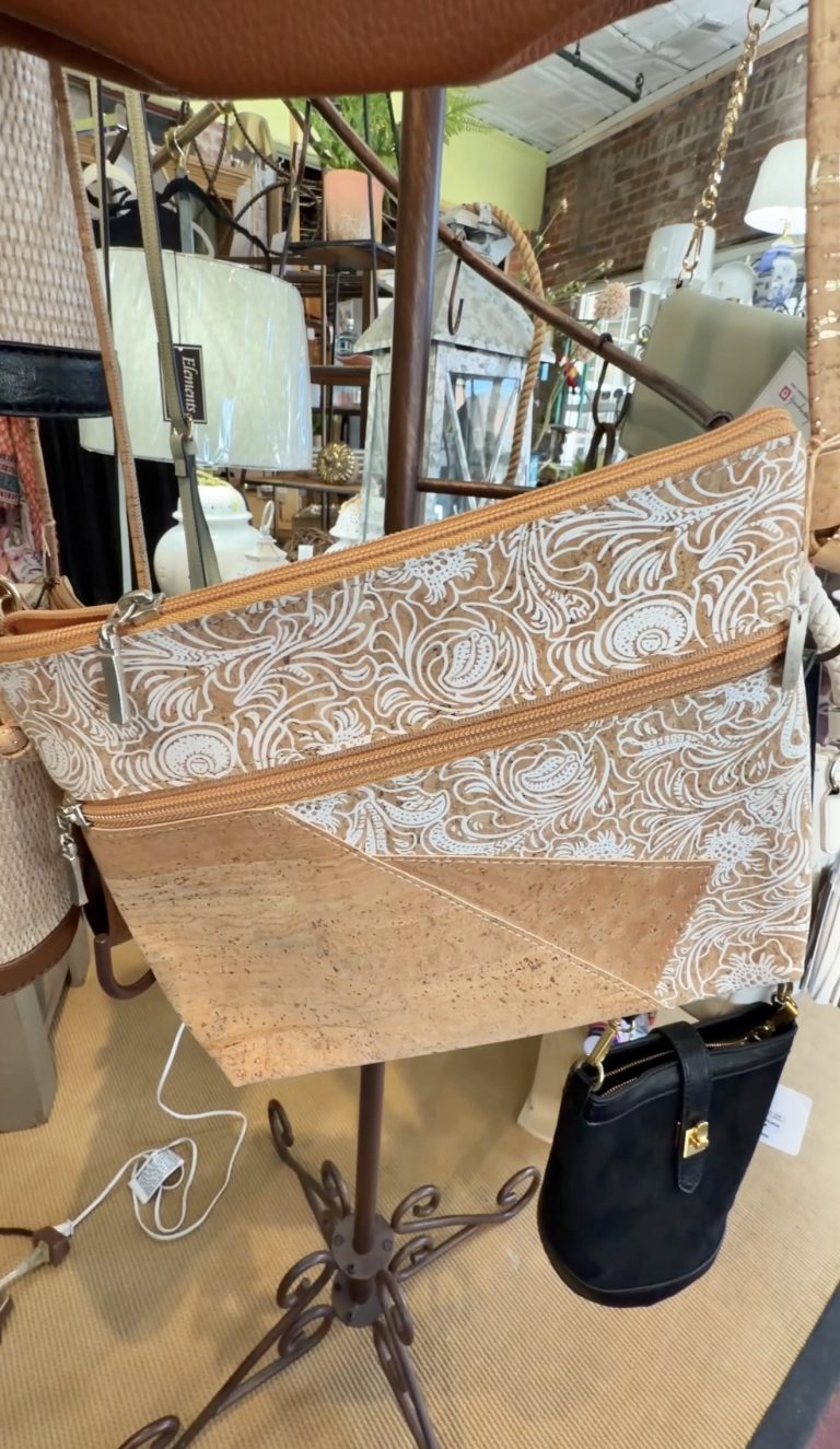 Paisley-patterned tan and white handbag with orange zippers on a display rack in a shop showroom.