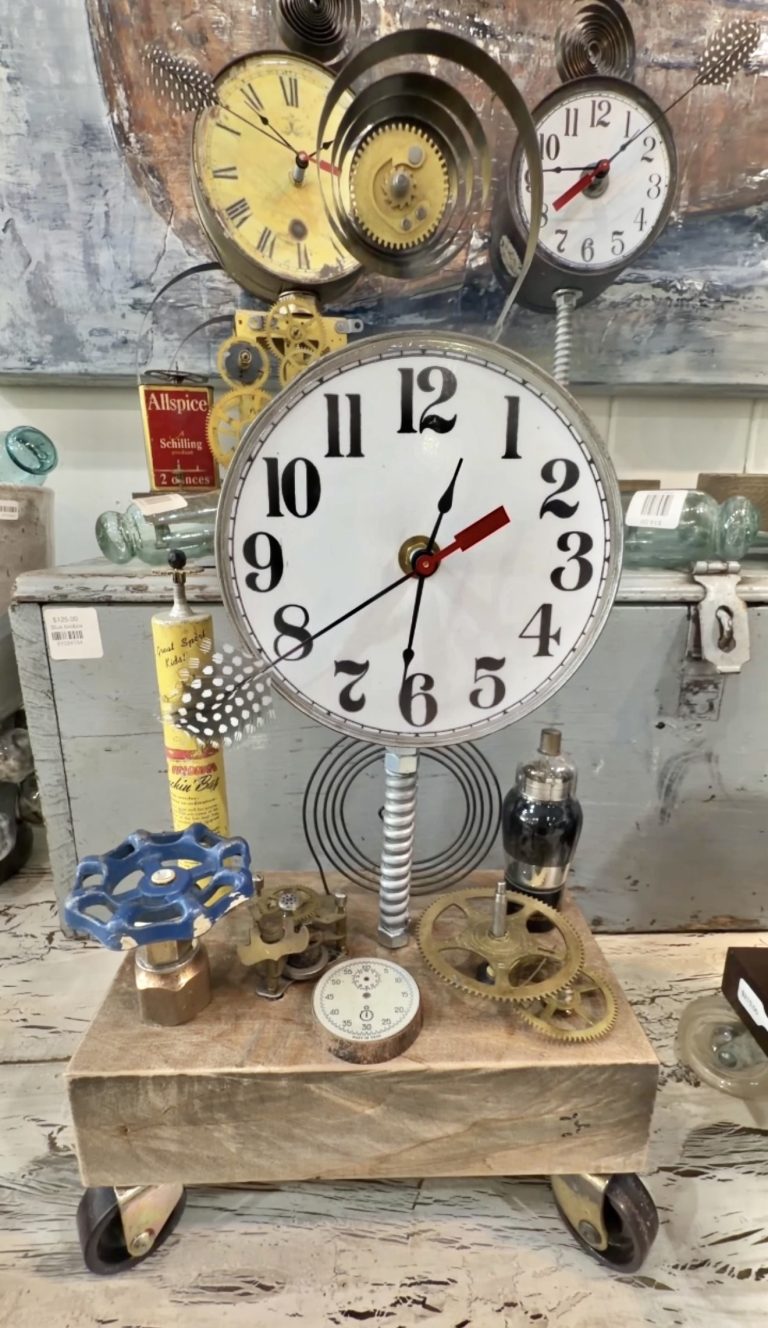 Steampunk clock sculpture with a large central clock and exposed brass gears on a wheeled wooden cart.