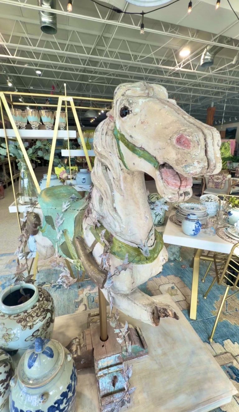Large weathered horse head sculpture in a bright showroom, surrounded by blue and white ceramic pots and plants.