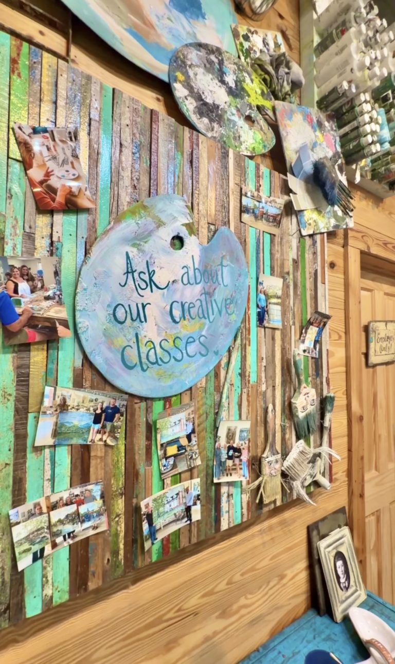 Colorful wooden slat wall with art supplies and photos, plus a round sign that says, 'Ask about our creative classes.'