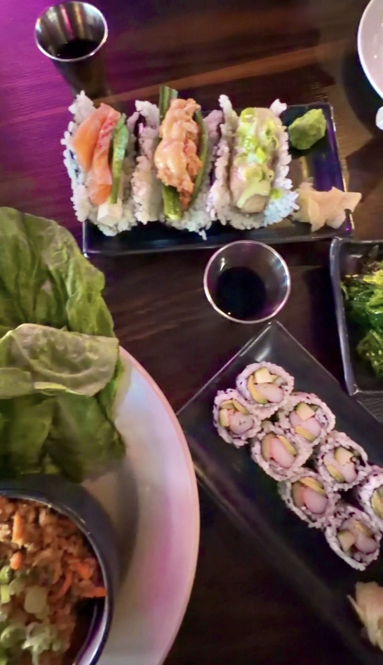 Assorted sushi rolls arranged on a rectangular plate with wasabi on the side and a small soy sauce cup nearby.