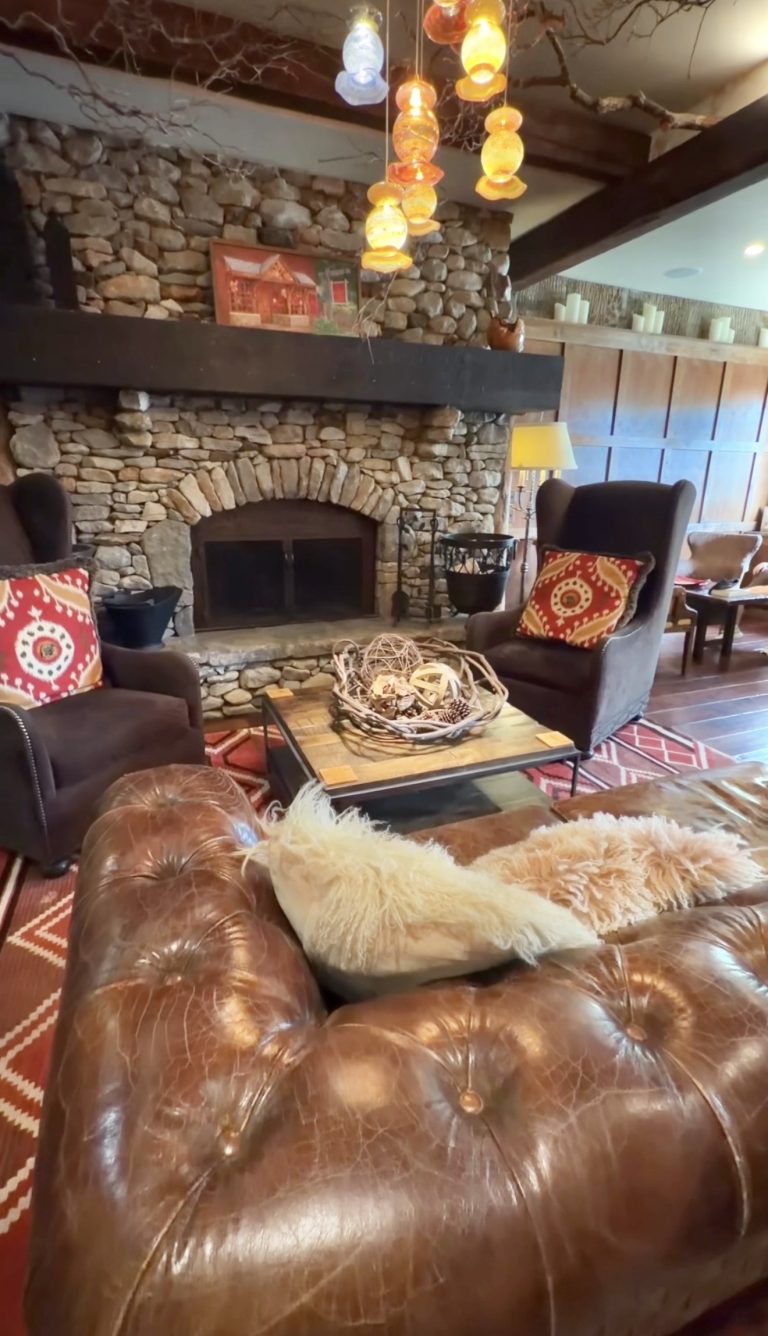 Cozy living room with a stone fireplace, leather sofa, and colorful hanging lanterns above a wooden coffee table.